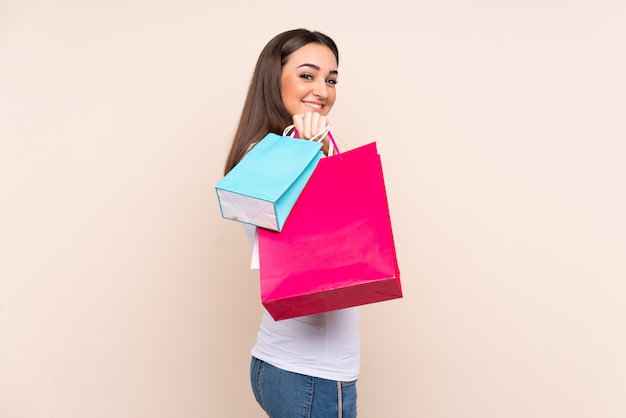 Young woman on beige holding shopping bags and smiling