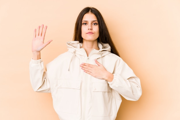 Giovane donna su beige prestando giuramento, mettendo la mano sul petto.