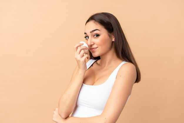 Young woman on beige with moisturizer and smelling it