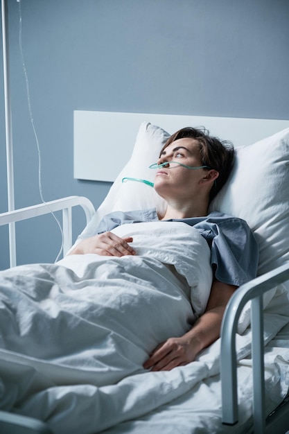 Young woman being treated at hospital, she lying on the bed with oxygen tube and looking away with pensive sight