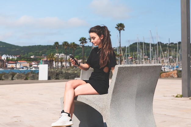 Photo young woman on a bench with a mobile phone at hendaia, basque country.