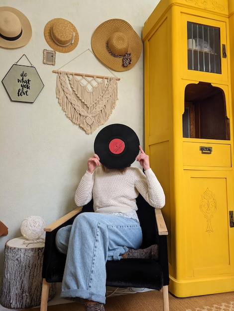 Young woman in beret sits in an armchair in cozy home, in room. music record. Vintage yellow cabinet