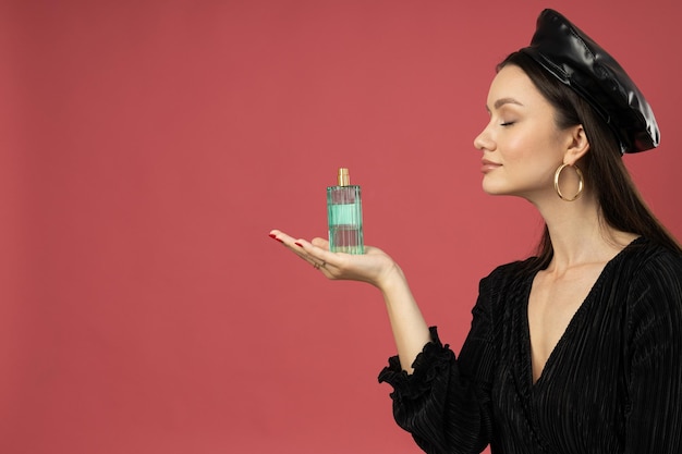 Photo young woman in beret with perfume bottle on pink background space for text