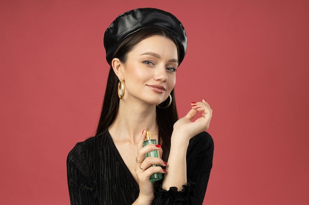 Young woman in beret with perfume bottle on pink background