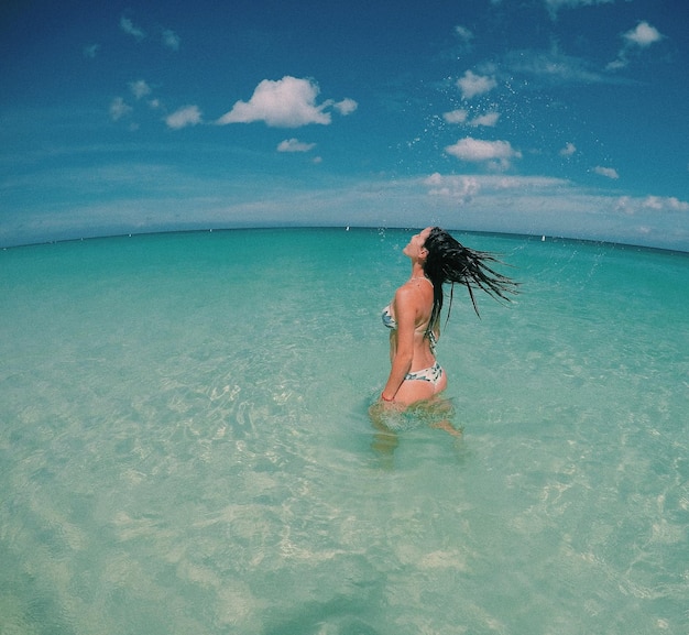 Foto giovane donna in bikini in piedi in mare contro il cielo