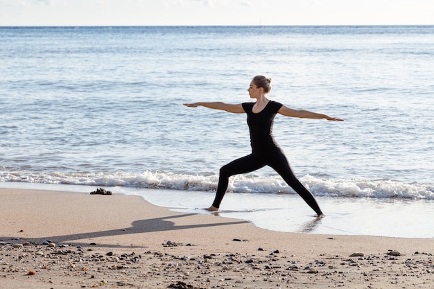 Young woman in black doing yoga on sand beach