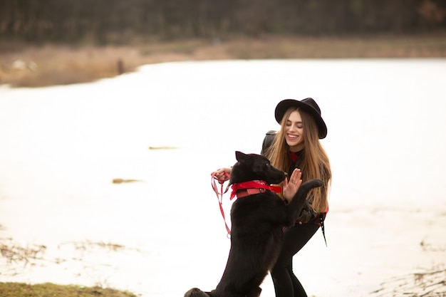 Молодая женщина в черной шляпе развлекается со своей собакой