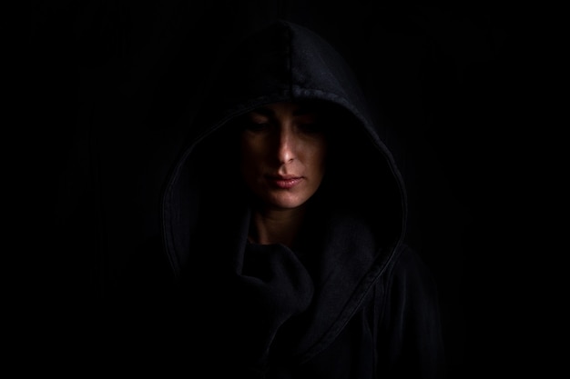 Young woman in a black hood on a dark black background.