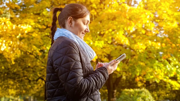 Young woman in a black jacket and a gray scarf is typing a message on the phone