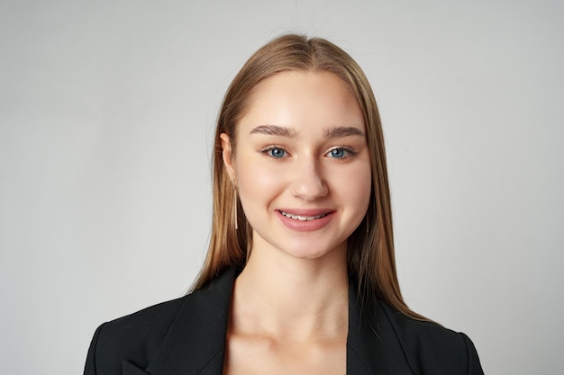 Young woman in black jacket posing to camera against gray background