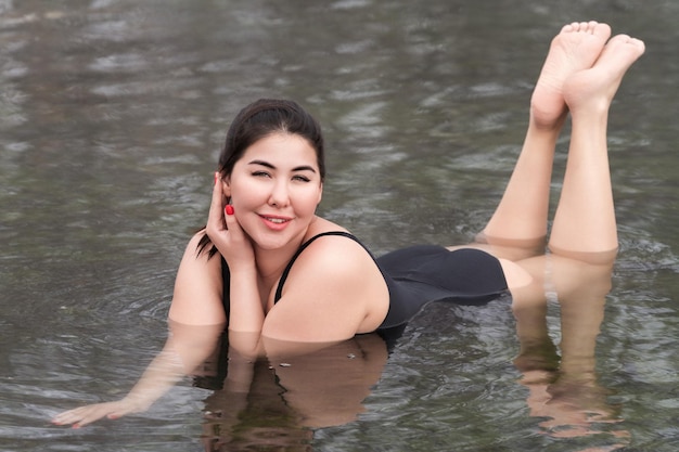 Young woman in black onepiece bathing swimsuit lying in outdoors pool at spa hot springs resorts