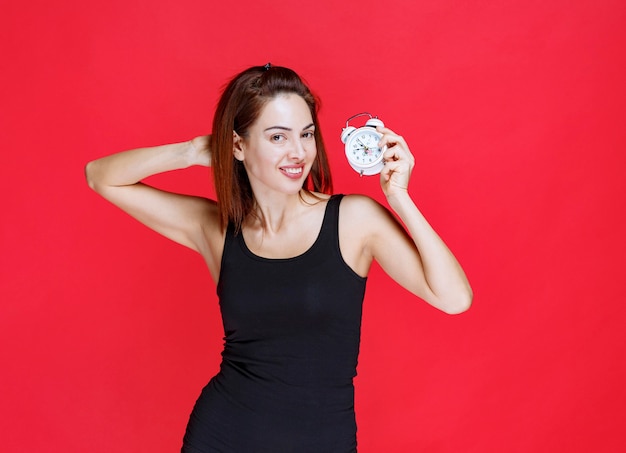 Young woman in black singlet holding an alarm clock and looks thoughtful