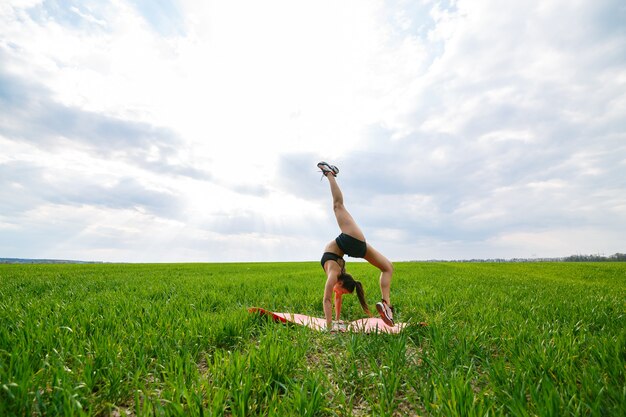 A young woman in a black top and shorts performs a handstand. a model stands on her hands, doing gymnastic splits against the blue sky. healthy lifestyle concept