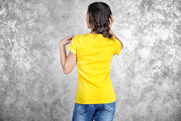 Young woman in blank yellow t-shirt standing against grey textured wall