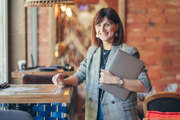 Giovane donna in blazer con net-book portatile nella caffetteria vicino alla finestra. professioni è una blogger, freelance e scrittrice.