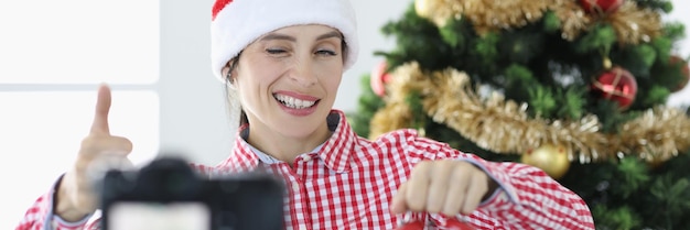 Young woman blogger in santa claus hat holds alarm clock and winks at camera new years
