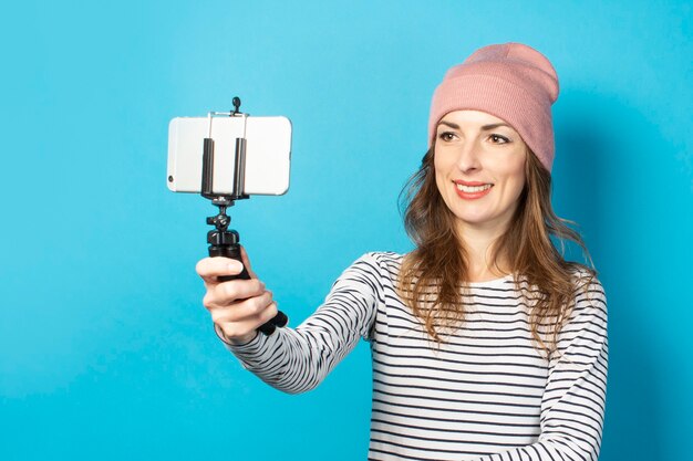 Young woman blogger takes pictures of himself on the phone on a blue surface