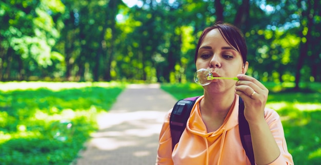 Young woman blowing bubbles on nature Happy young brunette woman strolls in the Park and makes soap bubbles on a Sunny day