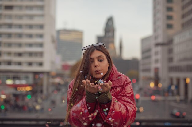 Young woman blowing colorful confetti in city during sunset