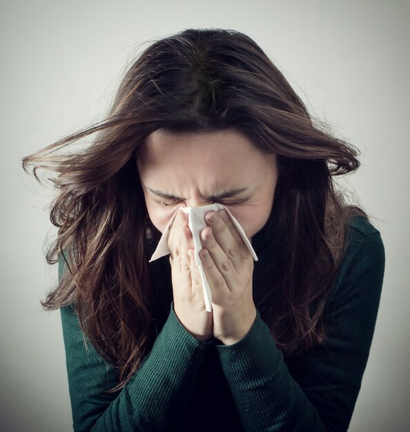 Young woman blowing her nose with paper tissue.