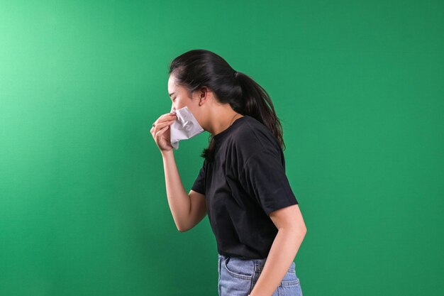 緑色の背景でティッシュに鼻を吹く若い女性