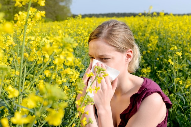 Young woman blowing nose while sitting against plants