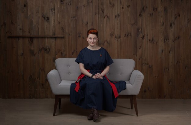 Young woman in a blue dress posing in the studio on a gray sofa.