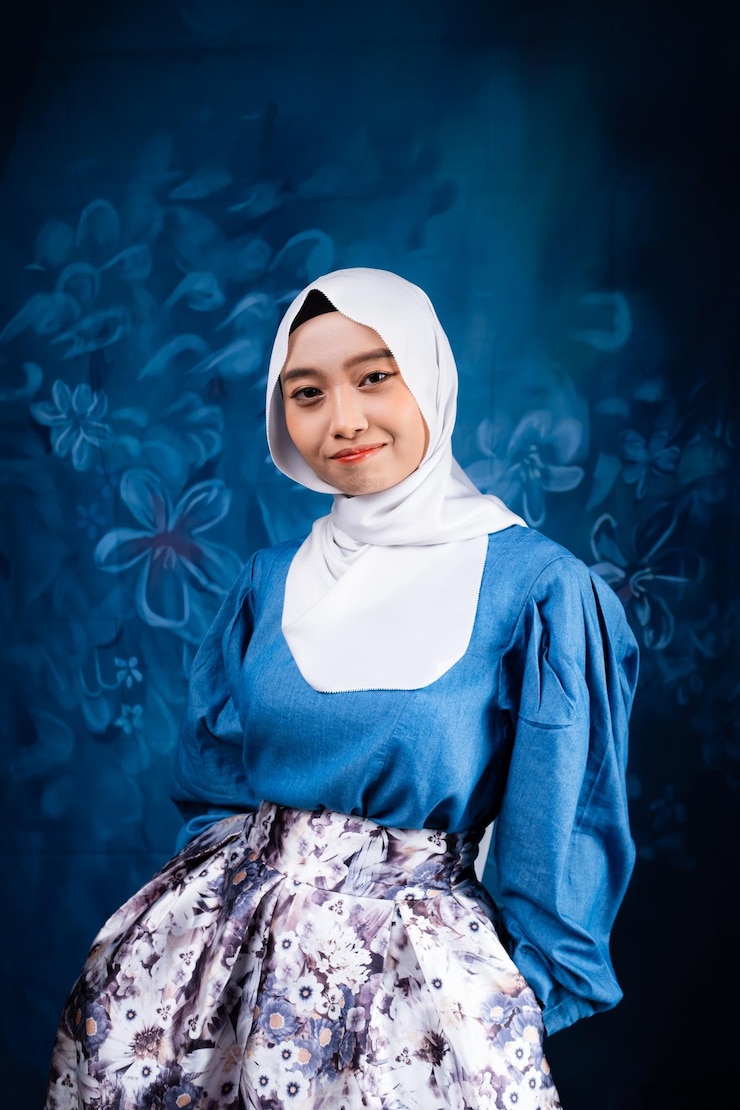 Photo a young woman in a blue dress and a white scarf is sitting in front of a blue background.