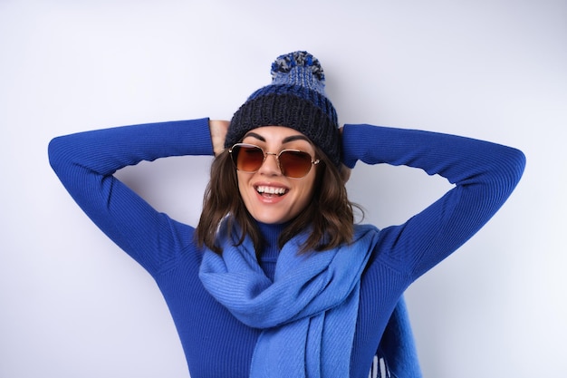 Giovane donna con un cappello da golf blu a collo alto e occhiali da sole sciarpa su uno sfondo bianco allegro di buon umore