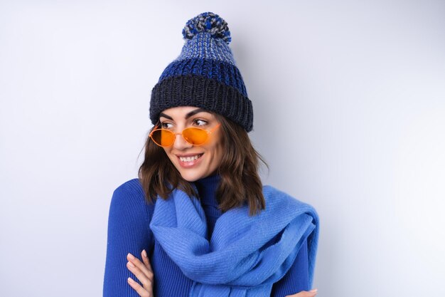 Young woman in a blue golf turtleneck hat and scarf sunglasses\
on a white background cheerful in a good mood