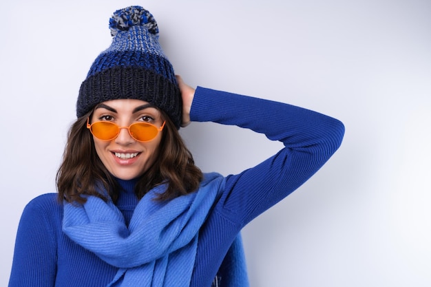 Young woman in a blue golf turtleneck hat and scarf sunglasses\
on a white background cheerful in a good mood