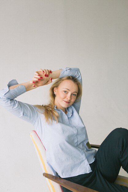 Foto giovane donna in camicia blu che si siede sulla sedia su fondo bianco