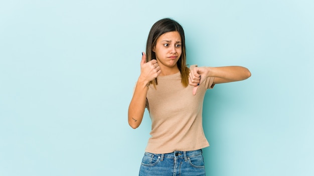 Young woman on blue showing thumbs up and thumbs down, difficult choose concept