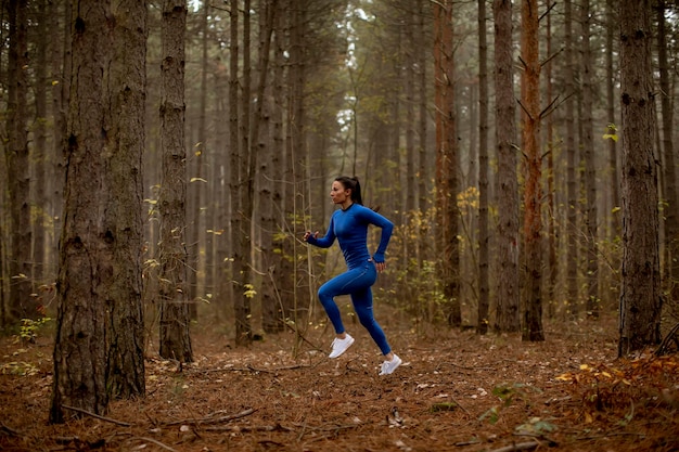 Young woman in blue track suit running on the forest trail at autumn