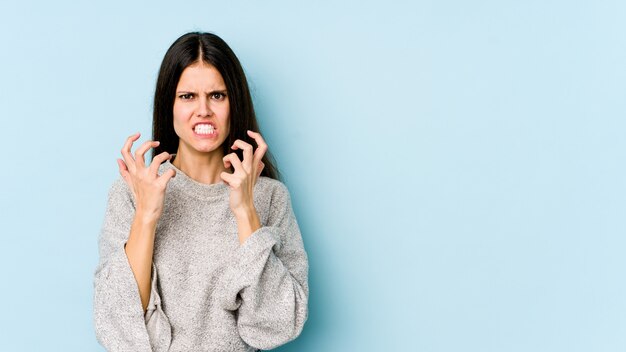 Young woman on blue upset screaming with tense hands.