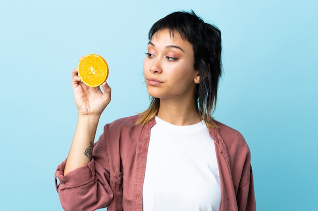 Young woman over blue wall holding an orange