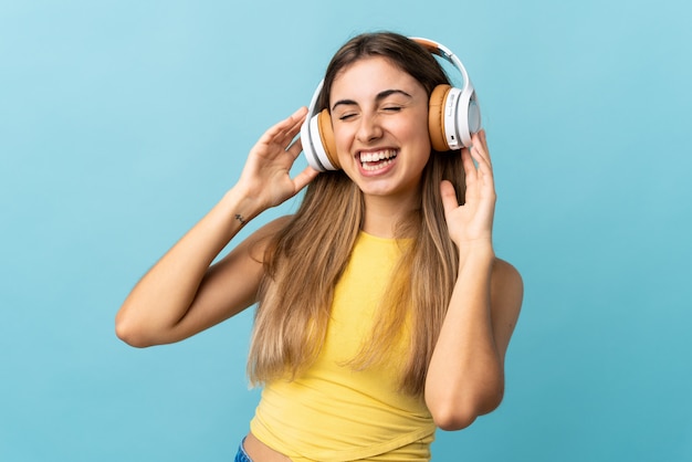 Young woman over blue wall listening music and singing