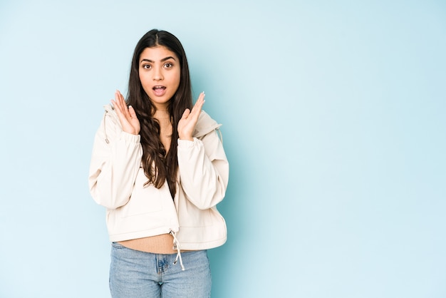 Young woman on blue wall surprised and shocked