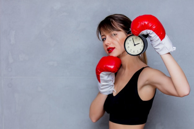 Young woman in boxing gloves with alarm clock 