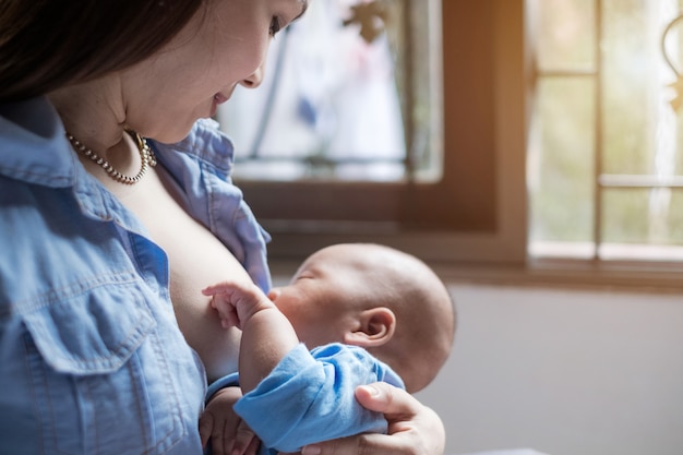 若い女性が自宅で彼女の赤ん坊を母乳で育てる。きれいな女性の母乳で育てる子供