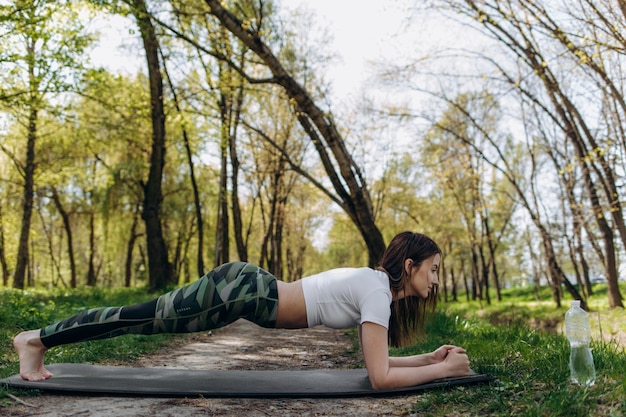 緑の自然公園の背景にヨガのポーズで呼吸する若い女性