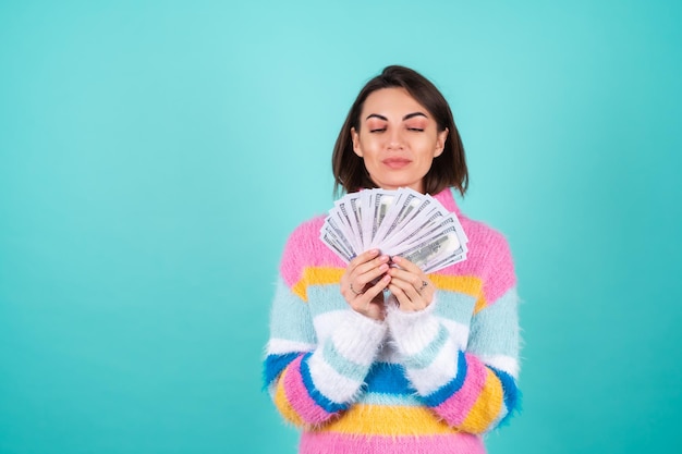 Young woman in a bright multicolored sweater on blue holds a bundle of dollars
