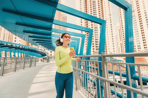 Young woman in bright sportswear quickly runs across a pedestrian bridge in the Dubai Marina district The concept of a female healthy lifestyle and fitness