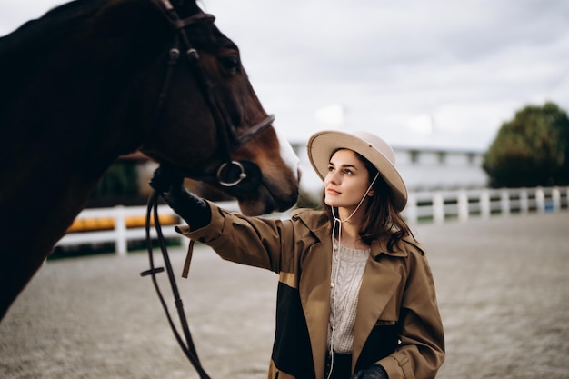 A young woman in a brown coat and hat near a horse