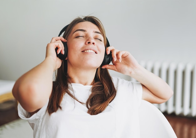 ヘッドフォンで音楽を聴いている白いTシャツのそばかすのある若い女性の茶色の髪と緑の目