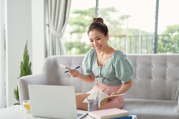 Young woman browse internet noting something relaxing on sofa