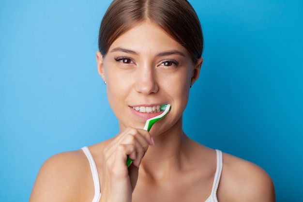 Young woman brushing her teeth on blue background