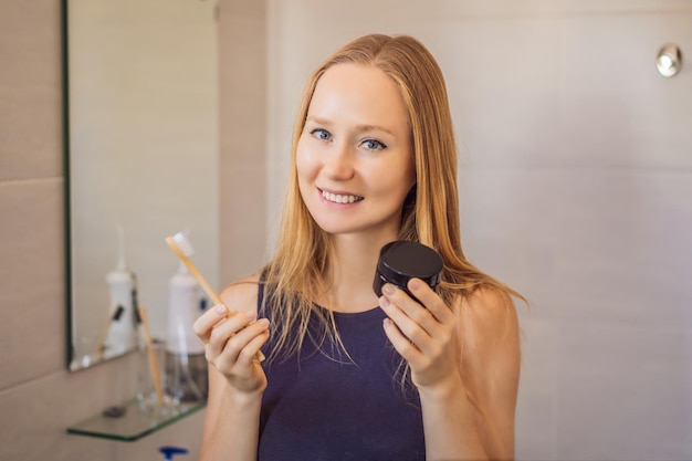 Young woman brushing her teeth with a black tooth paste with active charcoal and black tooth brush