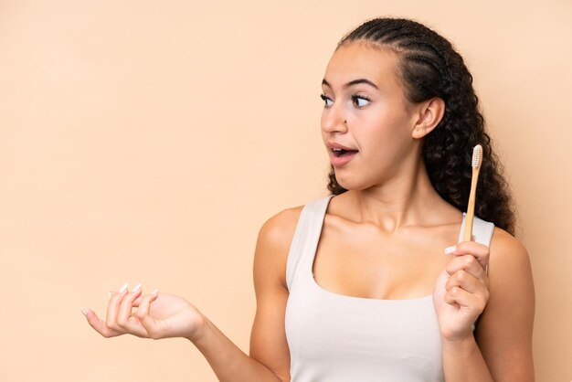 Young woman brushing teeth isolated on beige background with surprise facial expression