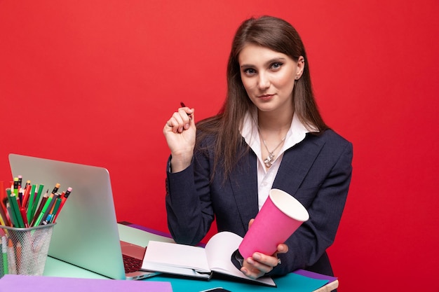 A young woman in business clothes writes down plans in a diary and drinks coffee